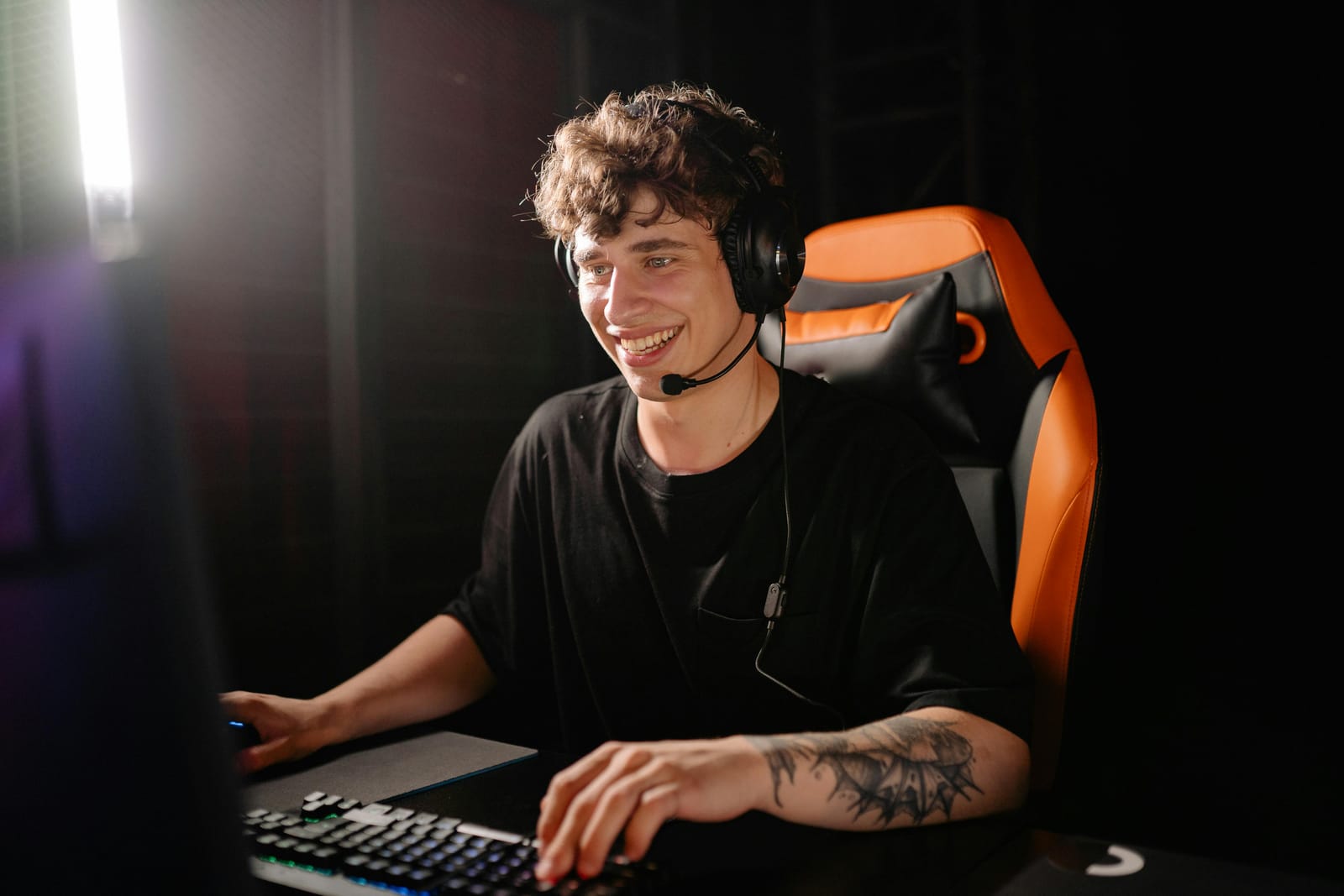 Smiling gamer with headset playing AAA games in a dark room